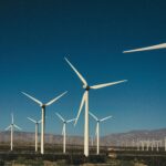 A vast landscape of wind turbines generating clean energy with a backdrop of mountains and a clear blue sky.